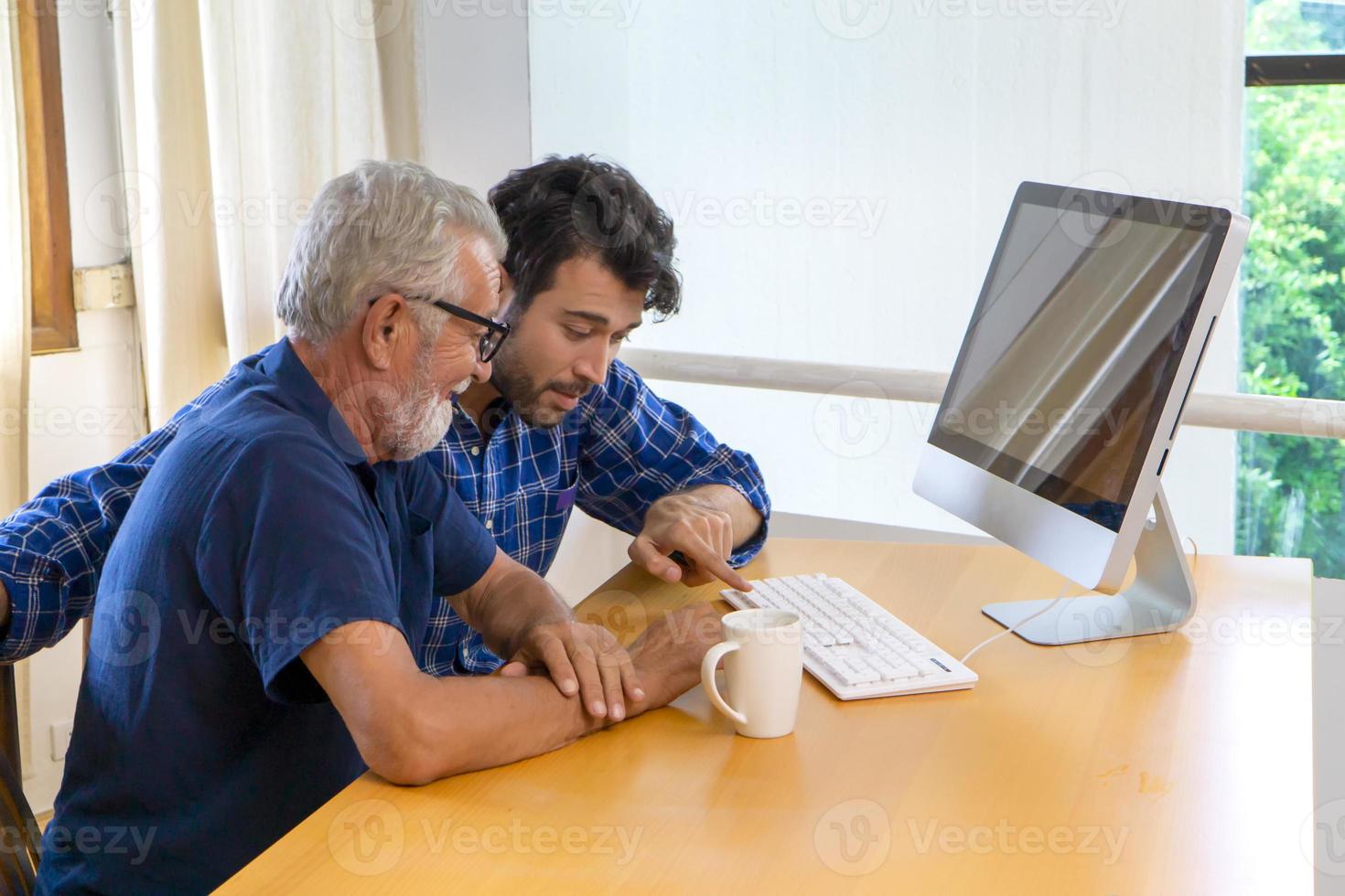 junger mann oder sohn, der seinem großvater, einem älteren vater, beibringt, zu hause computer zu benutzen. foto