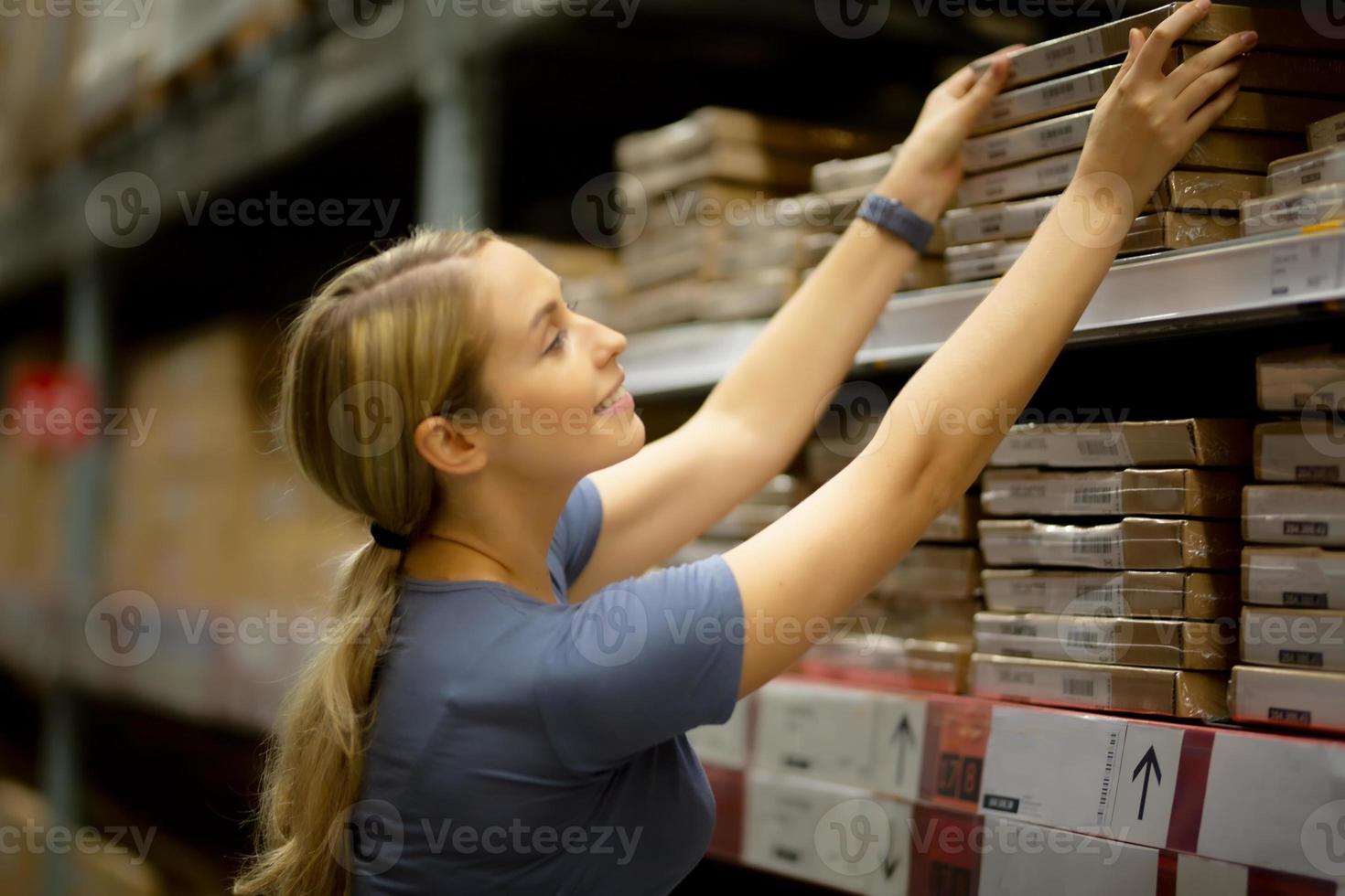 Fröhliche Kundin, die beim Einkaufen im Baumarkt nach oben schaut und Produkt ins Regal zieht foto