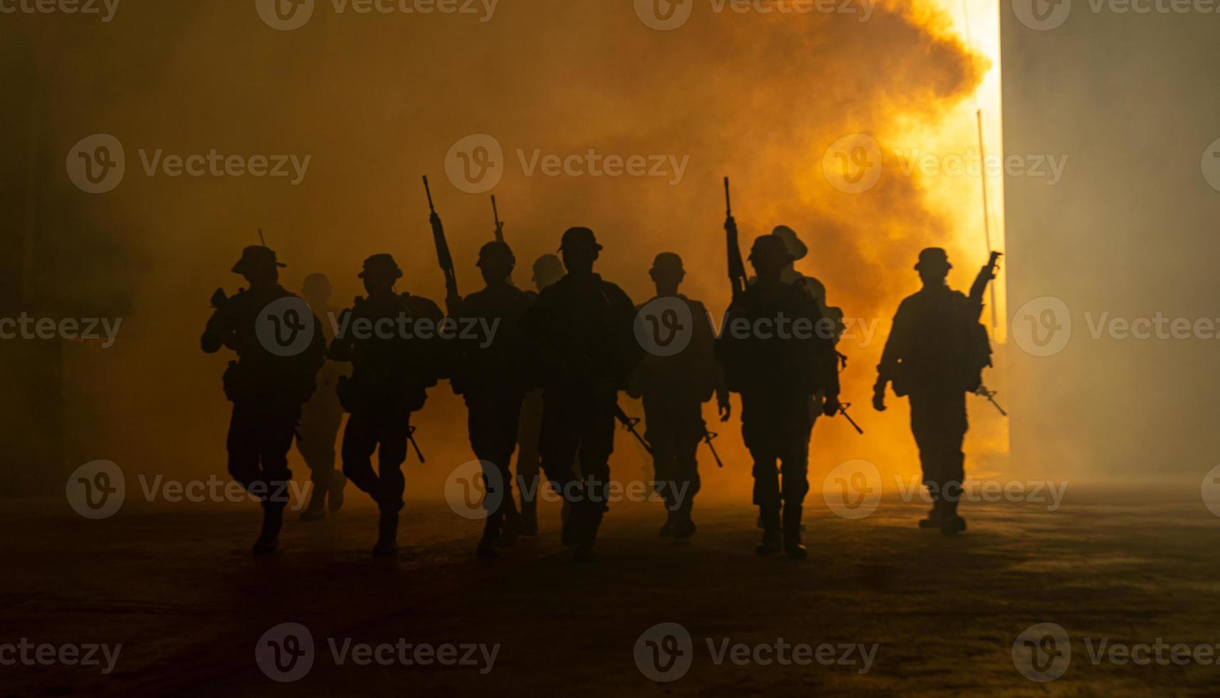 Silhouetten von Armeesoldaten im Nebel vor Sonnenuntergang, Marinesoldaten im Einsatz, Feuer und Rauch umgeben, mit Sturmgewehr und Maschinengewehr schießen, Feind angreifen foto