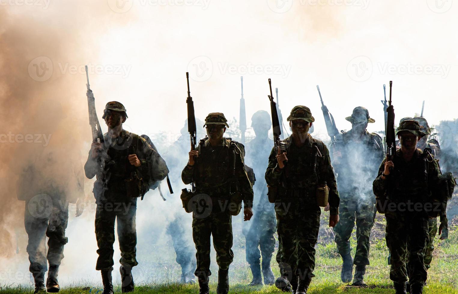 Silhouetten von Armeesoldaten im Nebel vor Sonnenuntergang, Marinesoldaten im Einsatz, Feuer und Rauch umgeben, mit Sturmgewehr und Maschinengewehr schießen, Feind angreifen foto