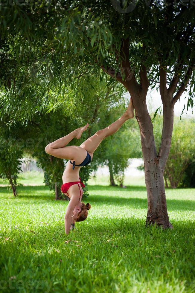 elegante badeanzugmodellfrau, die yoga auf grünem rasen tut foto