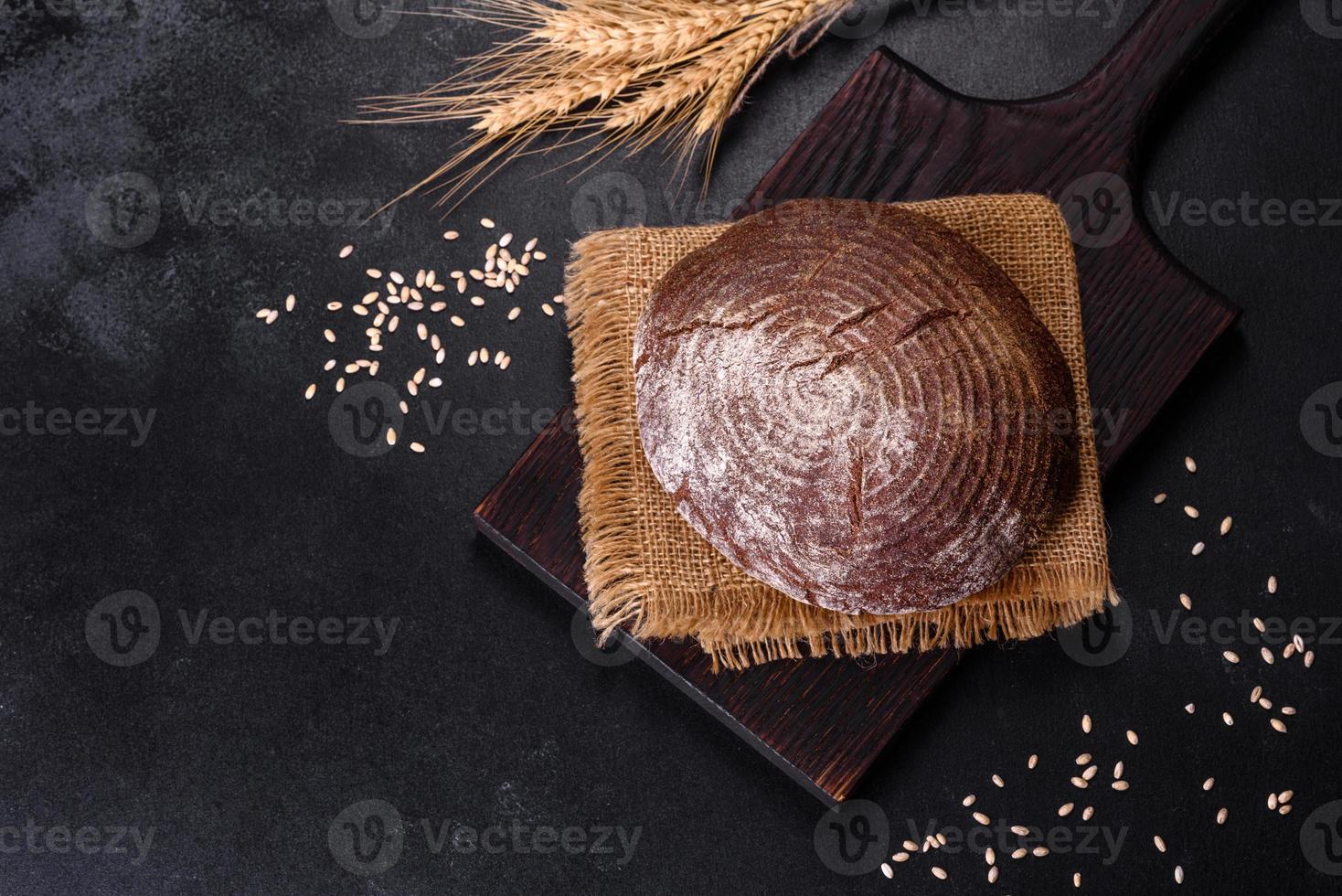 frisch gebackenes hausgemachtes Schwarzbrot auf schwarzem Betongrund mit Weizenkörnern foto