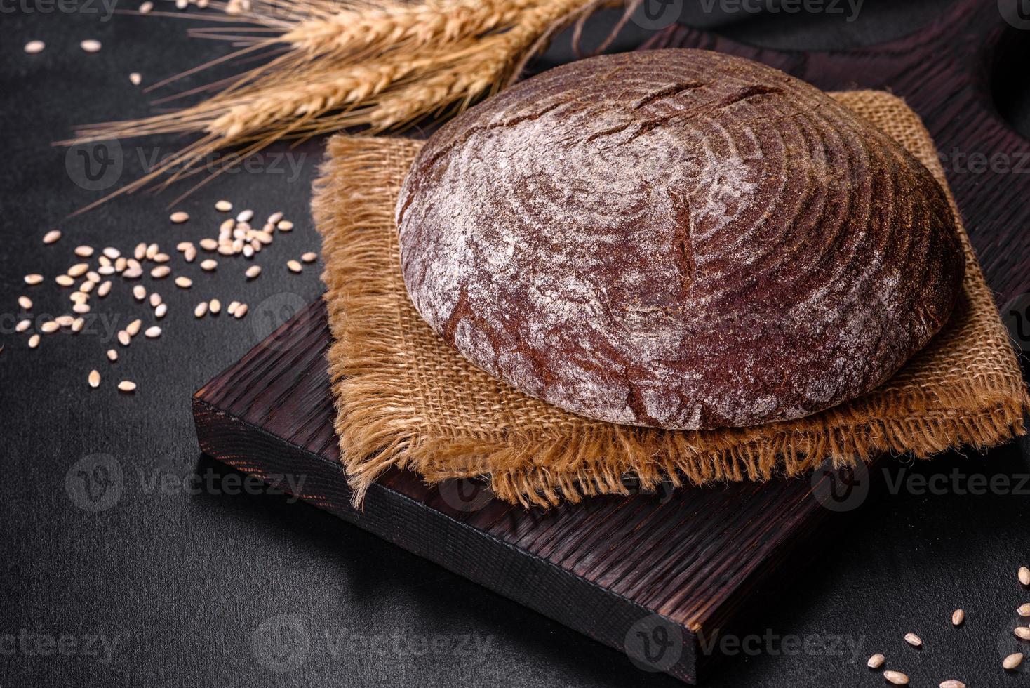 frisch gebackenes hausgemachtes Schwarzbrot auf schwarzem Betongrund mit Weizenkörnern foto