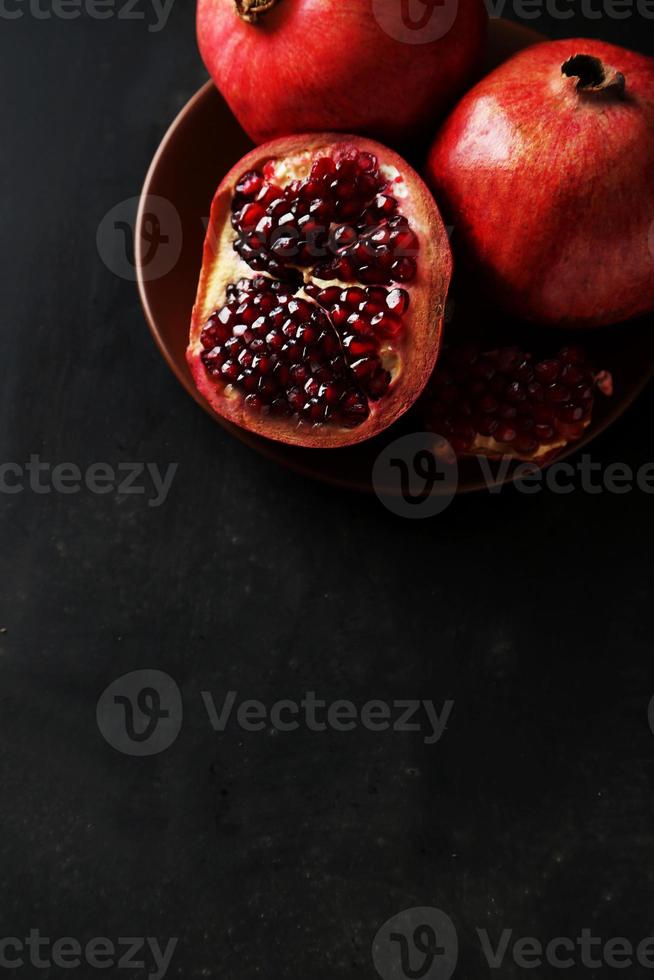 köstliche Granatapfelfrucht auf Platte auf schwarzem Hintergrund foto