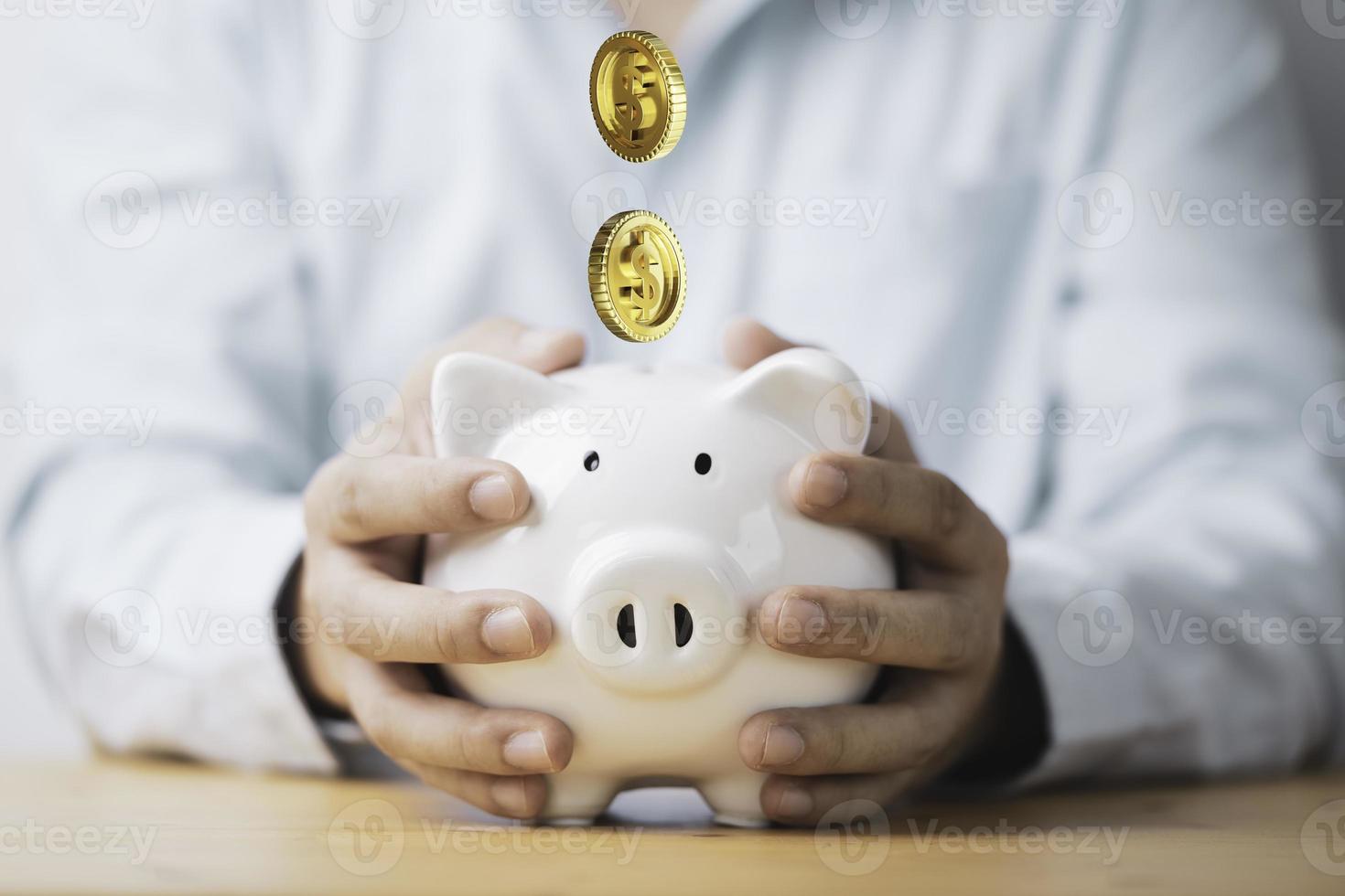 geschäftsmann, der weißes sparschwein hält, spart mit goldenen münzen, die auf einzahlungs- und geldsparinvestitionskonzept fallen. foto