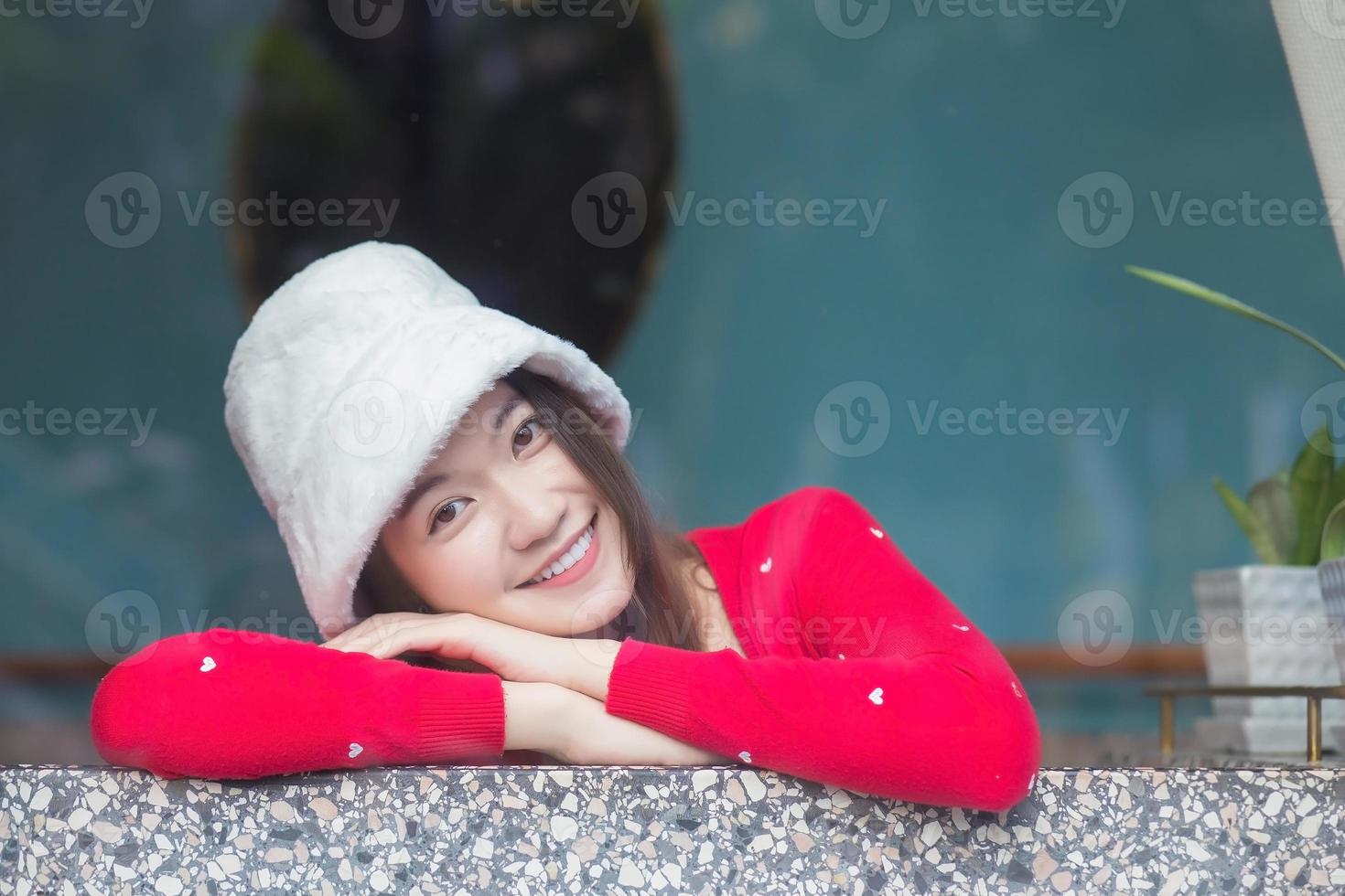 Portrait schöne Haut einer asiatischen Frau, die eine rote, langärmlige Strickjacke und einen cremefarbenen Hut trägt, lächelt glücklich und blickt in die Kamera. foto