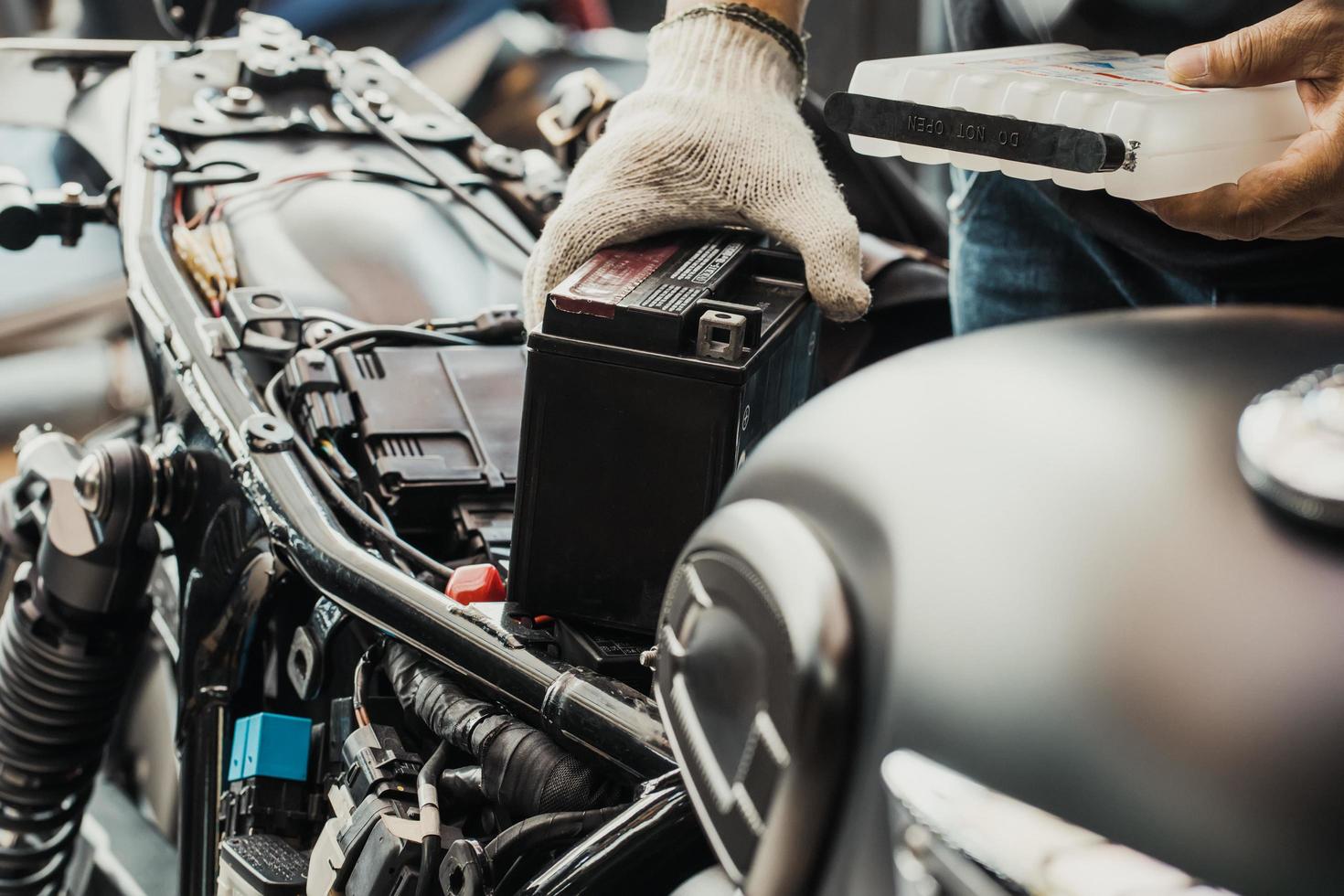 Der Mechaniker ersetzt die Motorradbatterie und hält ein Säurepaket oder ein versiegeltes Batterieelektrolytpaket, um das Auffüllen der Batterie, die Wartung des Motorrads sowie das Service- und Reparaturkonzept vorzubereiten. selektiver Fokus foto