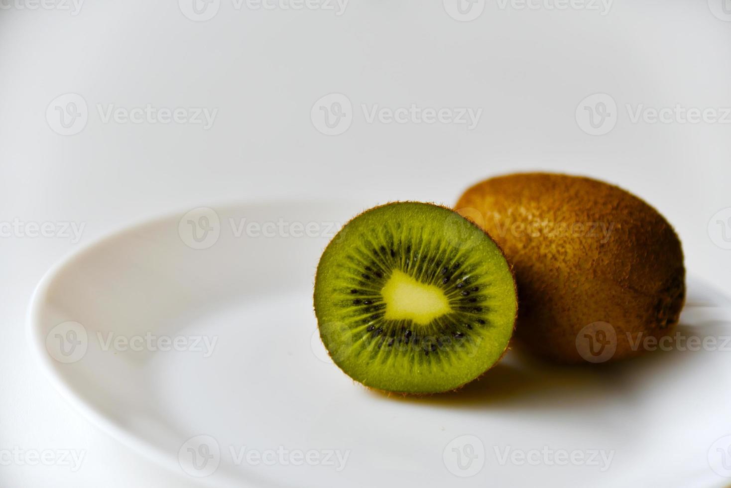 eine ganze Kiwi und die Hälfte auf einem weißen Teller foto