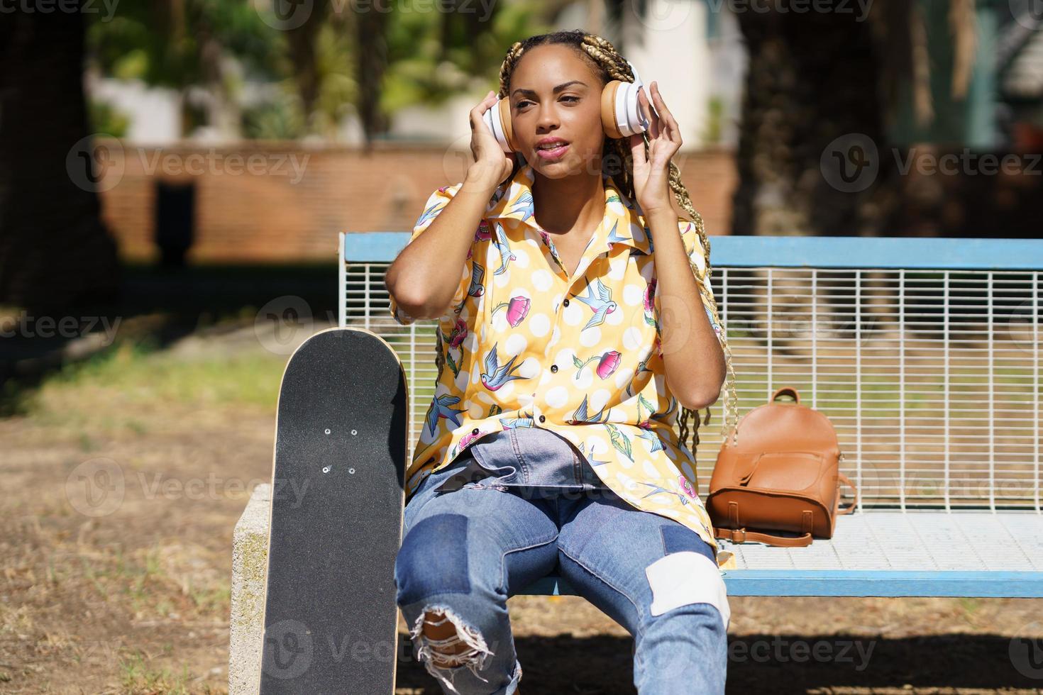 Afrikanisches Mädchen mit Skateboard, das sich entspannt, nachdem es Skateboard gefahren ist, um Musik zu hören foto