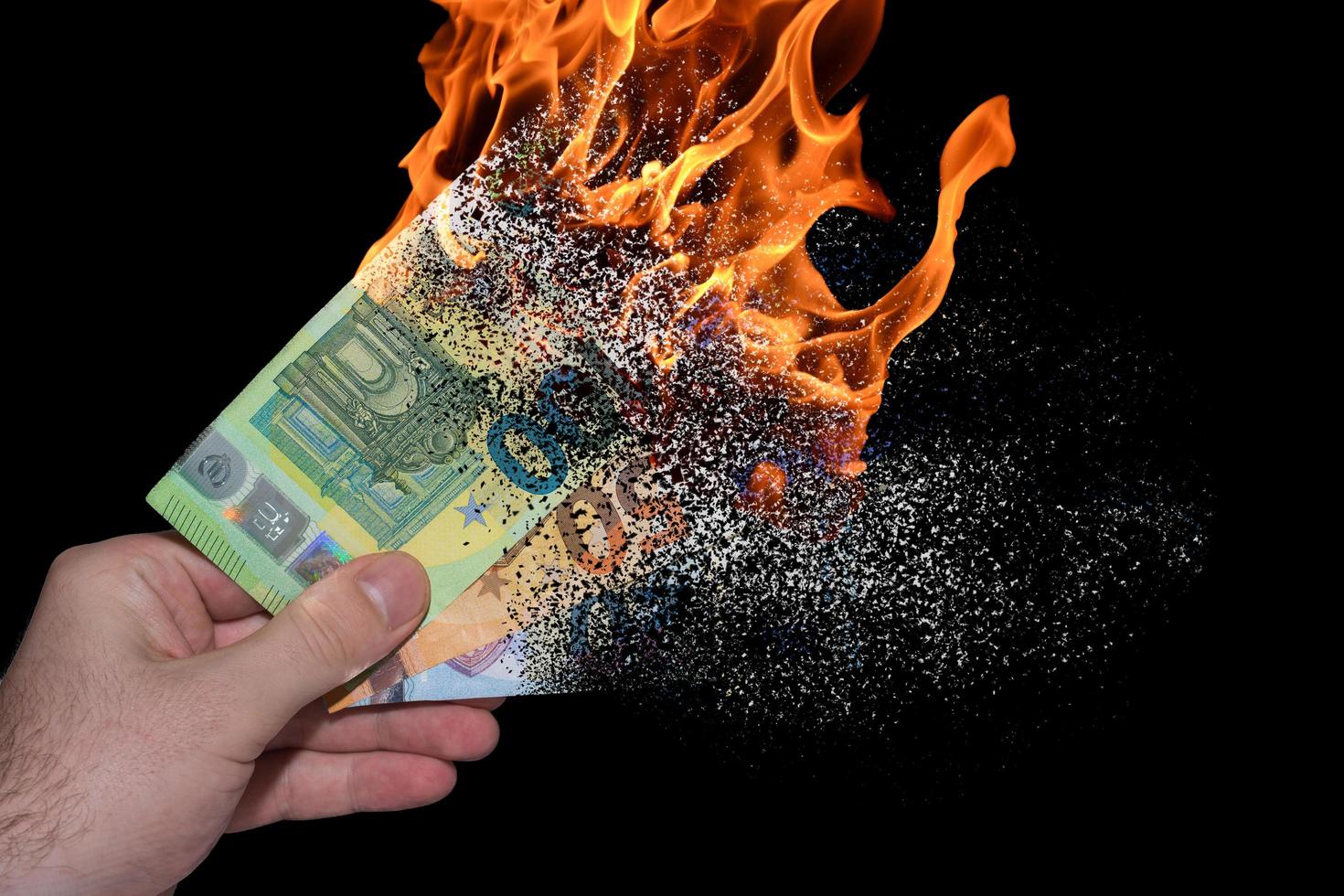 Drei brennende Euro-Banknoten, die in einer Hand gehalten werden, zersetzen sich und lösen sich aufgrund der Inflation mit Schwarz auf foto