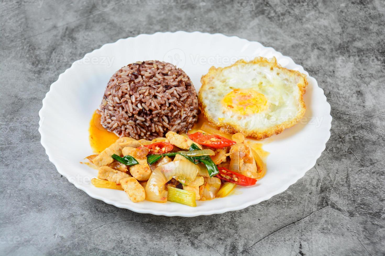 Gebratenes Hähnchen, süße Zwiebeln und Paprika, serviert mit braunem Reis und Spiegelei auf einem weißen Teller foto