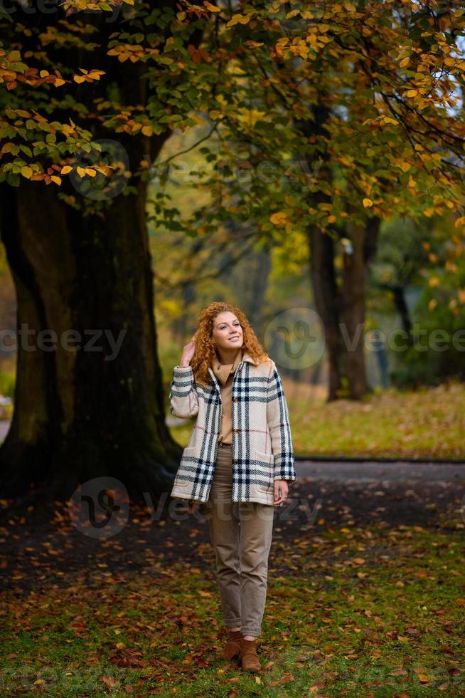 schönes rothaariges Mädchen mit lockigem Haar und blauen Augen. Das Mädchen trägt eine karierte Jacke. Das Mädchen sitzt auf einer Bank. foto