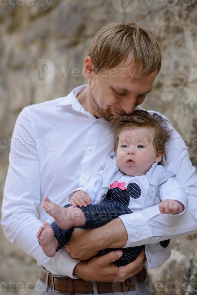 Porträt eines jungen Vaters, der ein weinendes Mädchen über einer weißen Backsteinmauer hält foto