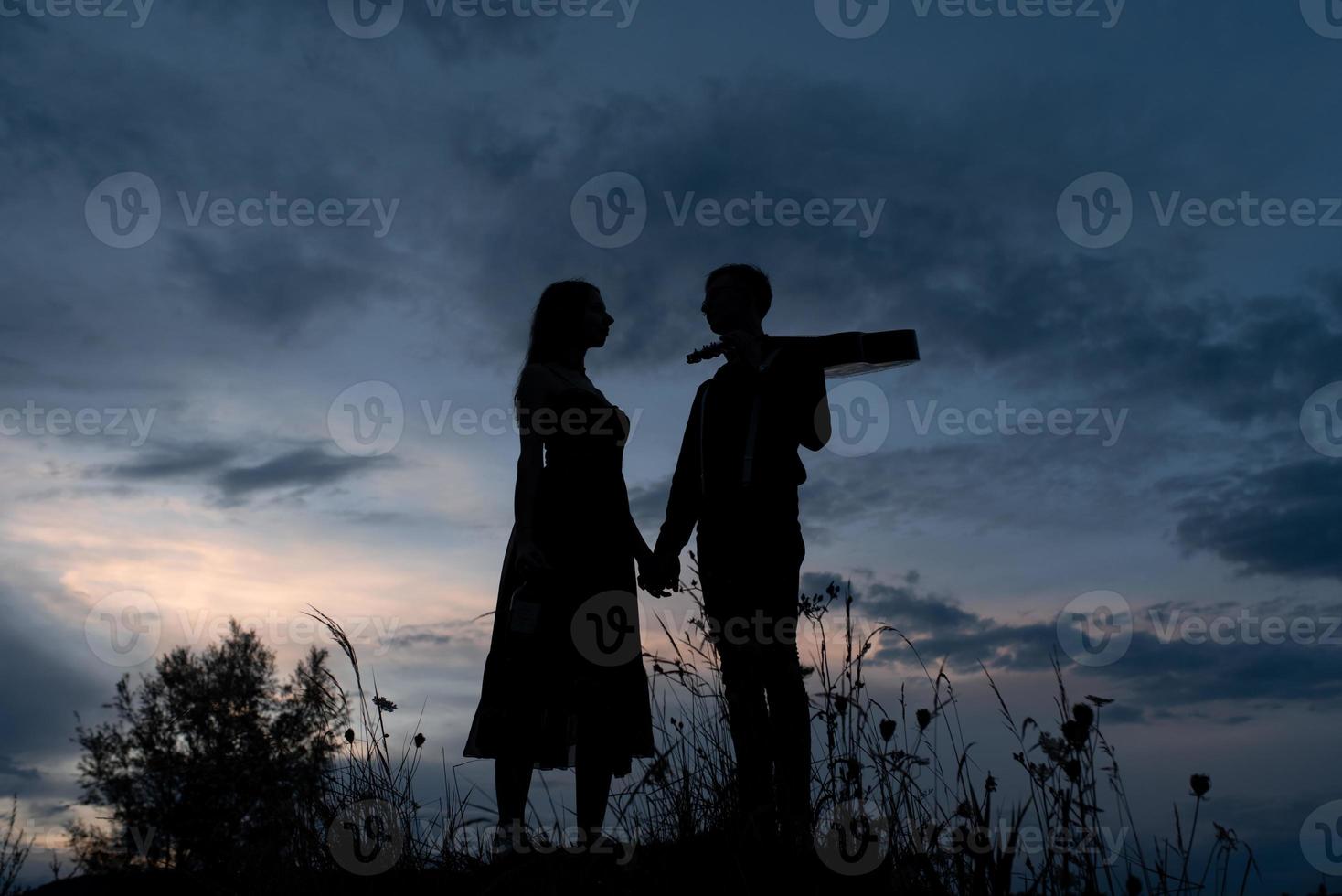 Silhouette eines verliebten Paares bei einem Date. Der Mann hält die Hand des Mädchens. der Typ in Krabben hat eine Gitarre. bei Sonnenuntergang gefilmt. foto