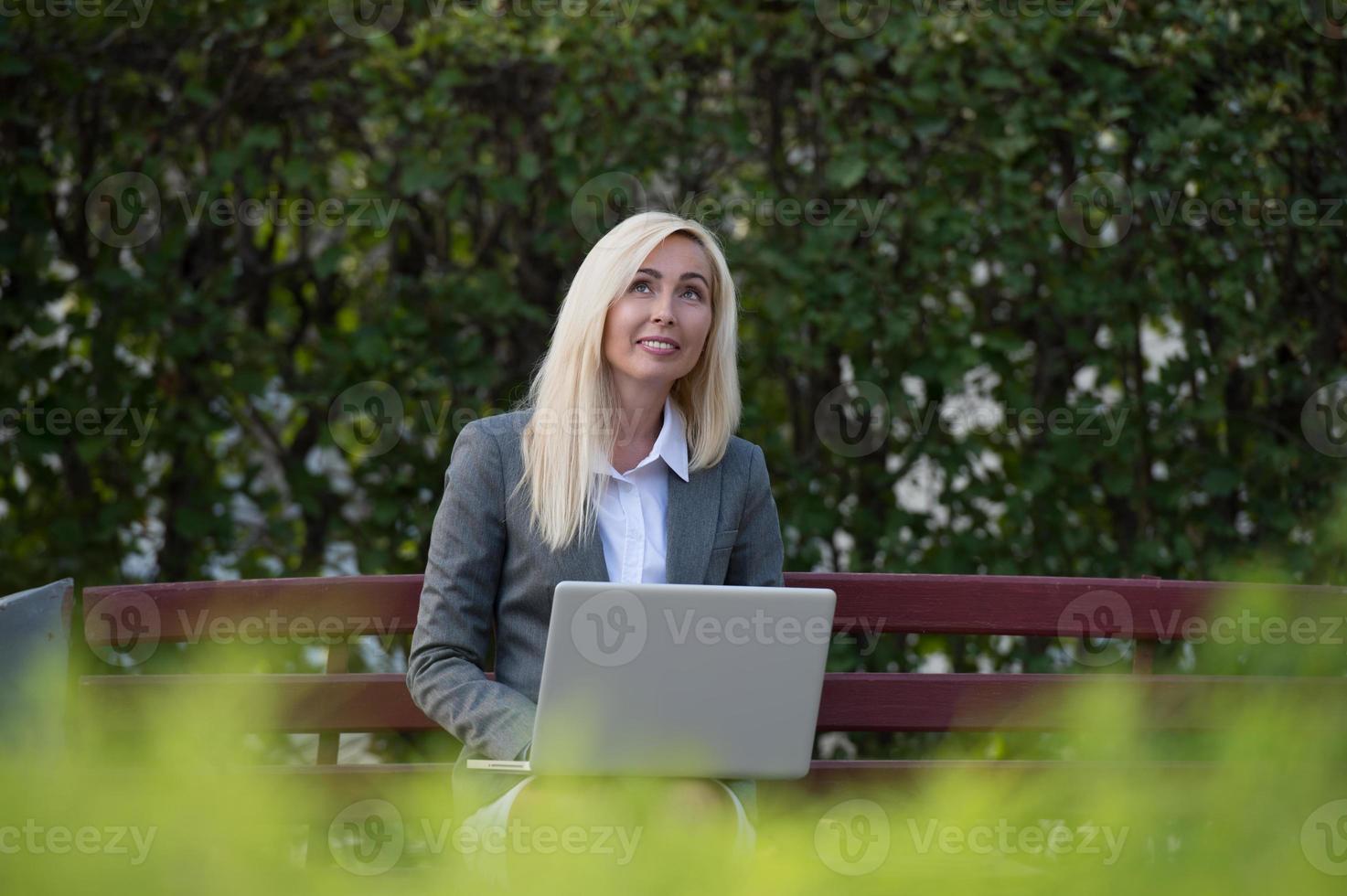 Geschäftsfrau im Park, der auf Bank sitzt und Laptop verwendet foto