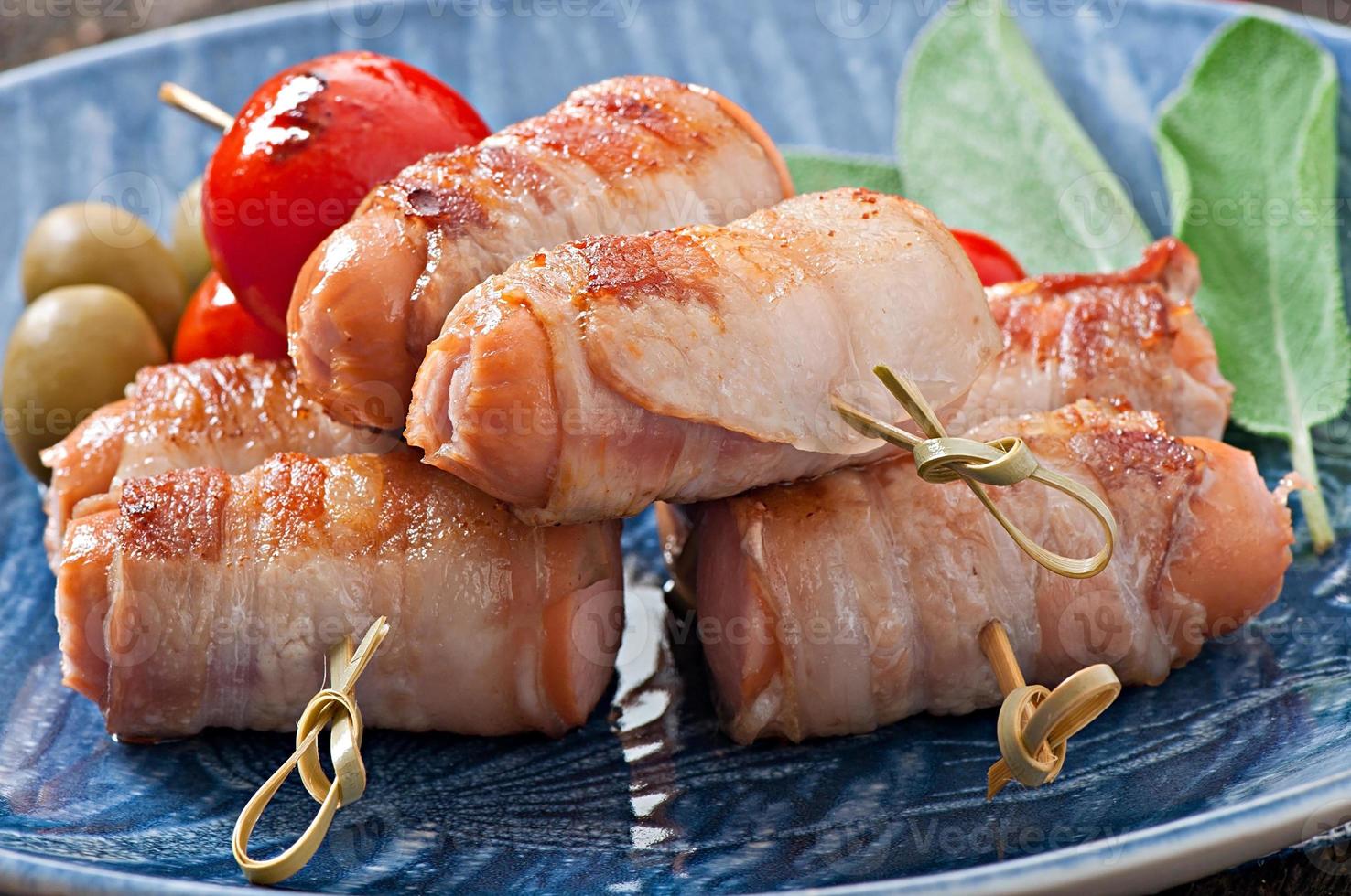 in Speckstreifen gewickelte Bratwürste mit Tomaten und Salbeiblättern foto