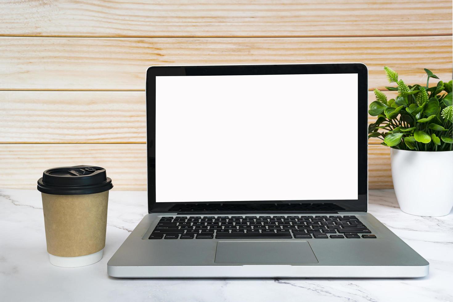 laptop oder notebook mit leerem bildschirm, kaffee und topfpflanze auf weißem tisch. foto