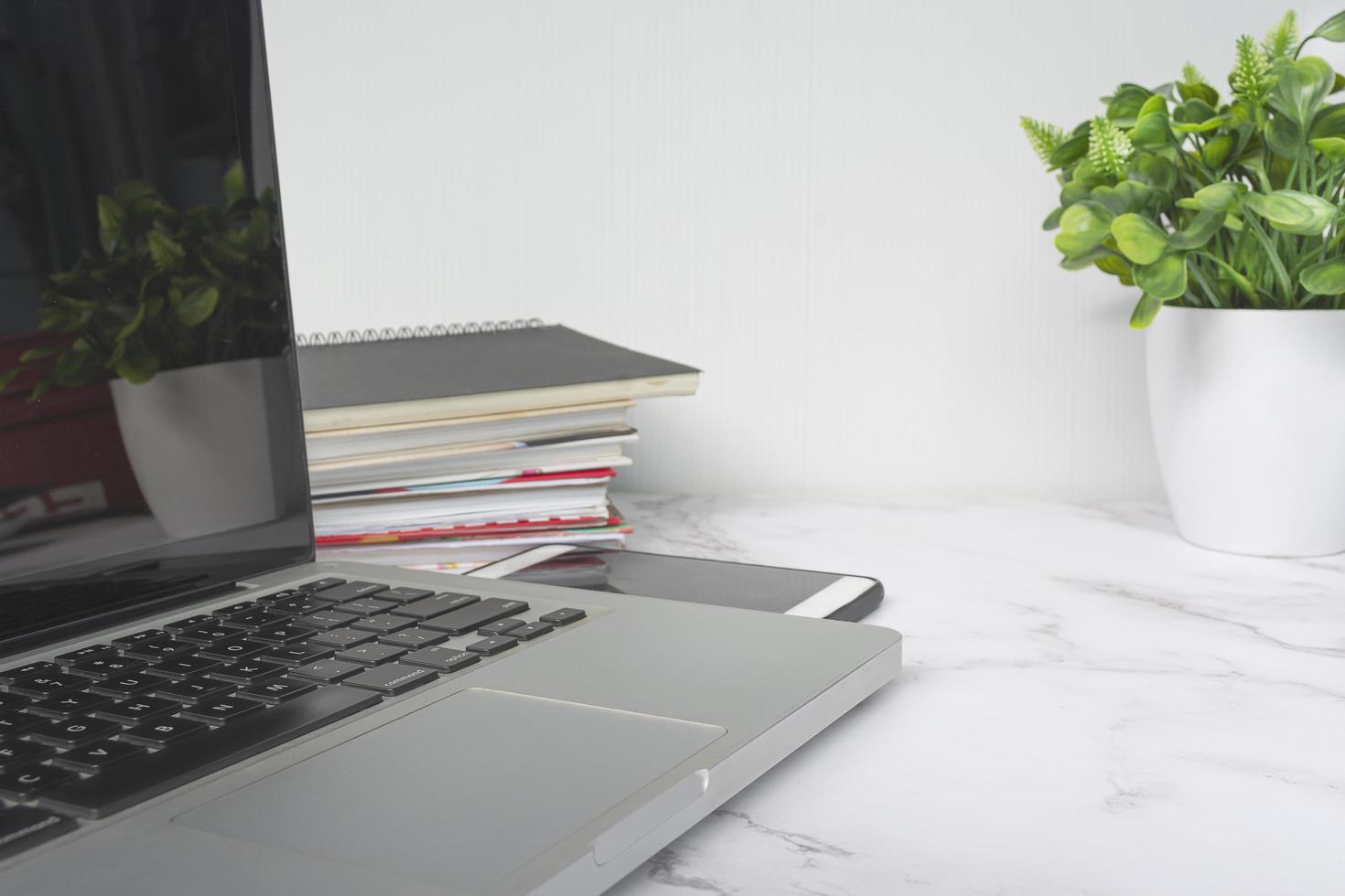 laptop auf weißem tisch mit topfpflanze, notebooks und smartphone. foto