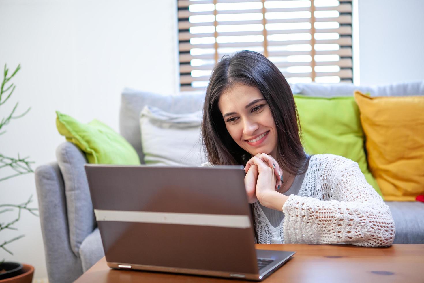 Schöne junge Frau, die am Laptop arbeitet, während sie im Wohnzimmer sitzt foto