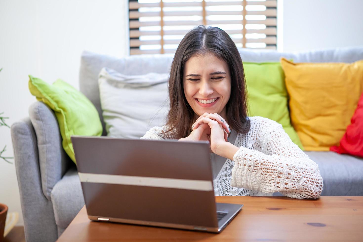 Schöne junge Frau, die am Laptop arbeitet, während sie im Wohnzimmer sitzt foto