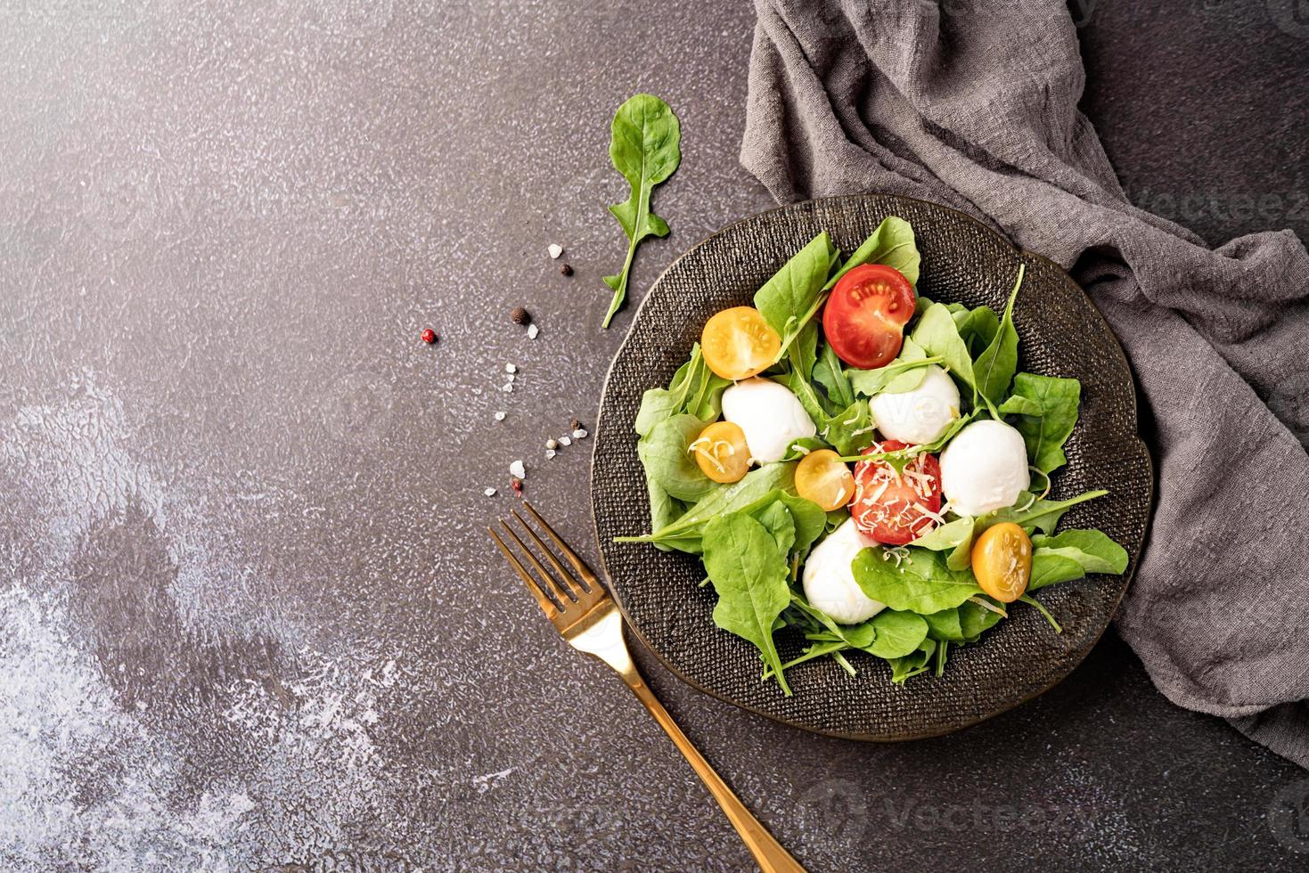 frischer Salat mit Rucola, Kirschtomaten, Mozzarella-Käse und Hartkäse auf dunklem Hintergrund. Ansicht von oben foto