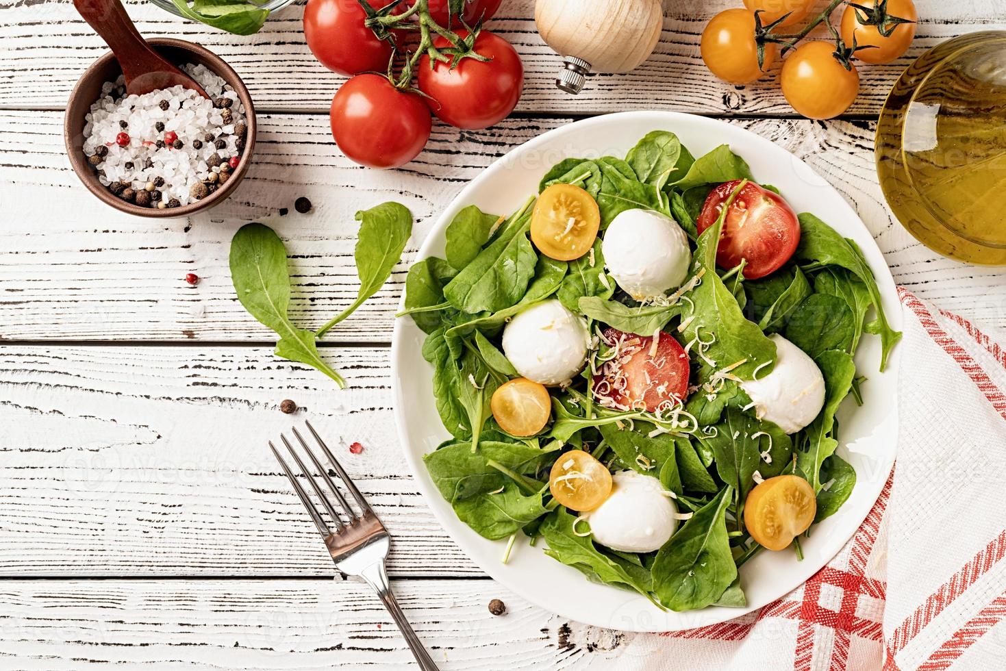 Frischer Salat mit Rucola, Kirschtomaten, Mozzarella-Käse und Hartkäse auf weißem Holzhintergrund. Ansicht von oben foto