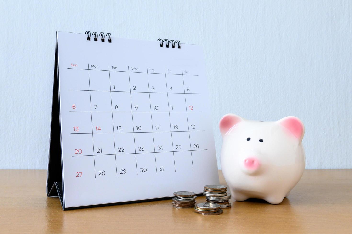 Kalender mit Tagen und Sparschwein auf Holztisch foto