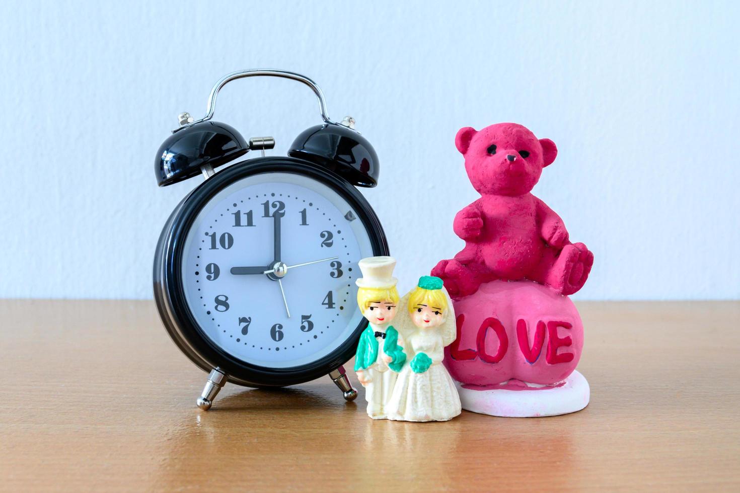 Miniatur-Ehepaar und Teddybär und Uhr auf Holz. konzept für den hochzeitsvalentinstag. foto