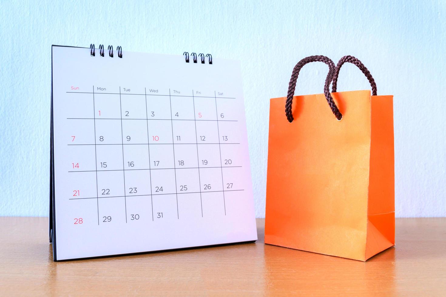 Kalender mit Tagen und orangefarbener Papiertüte auf Holztisch. Einkaufskonzept foto