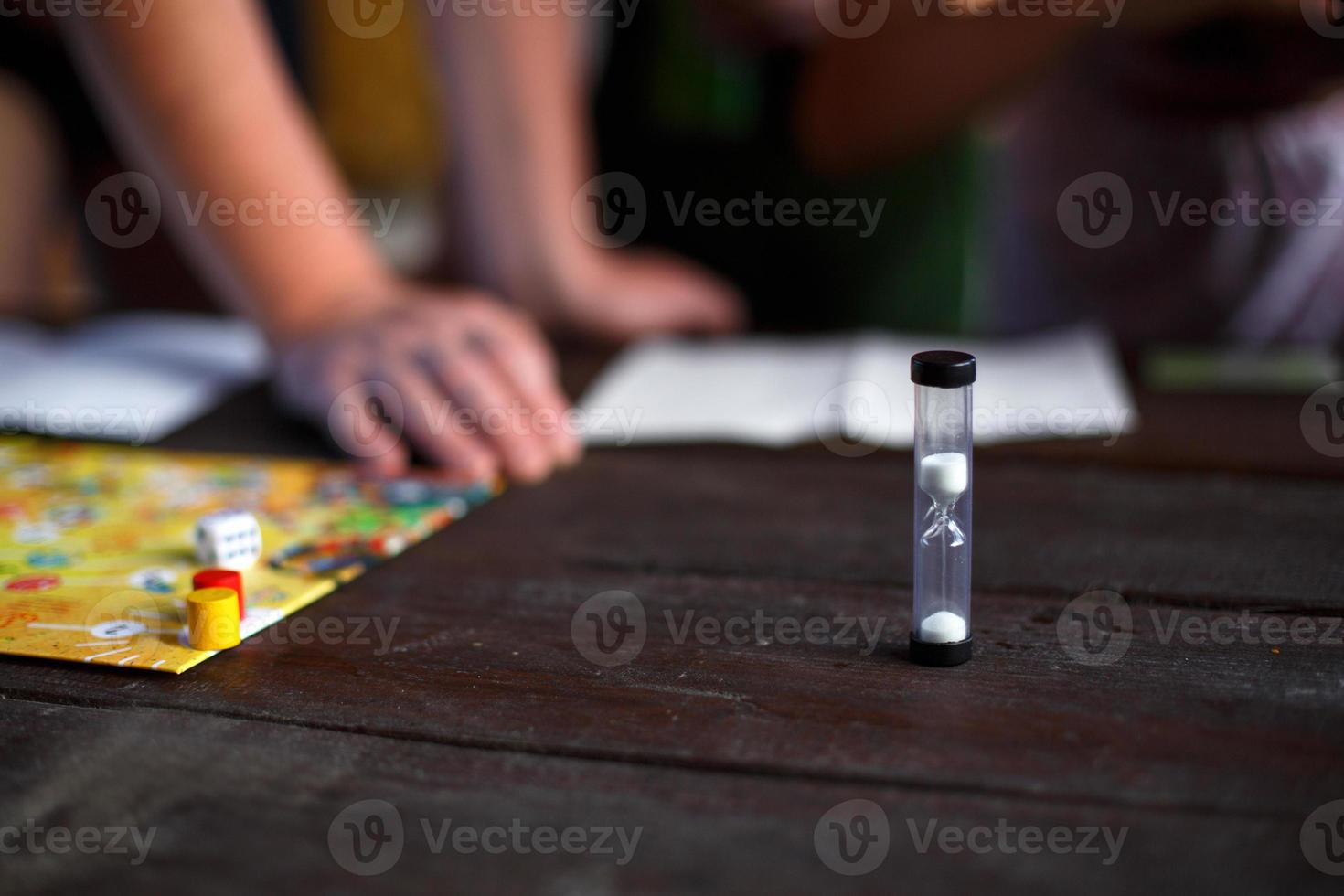 Brettspielbrett, Chips, Würfel, Timer auf einem dunklen Holztisch und Hände im Hintergrund. das konzept der teamarbeit, der intellektuellen entspannung, der firmenveranstaltung, des spielens zu hause mit kindern. Platz kopieren foto