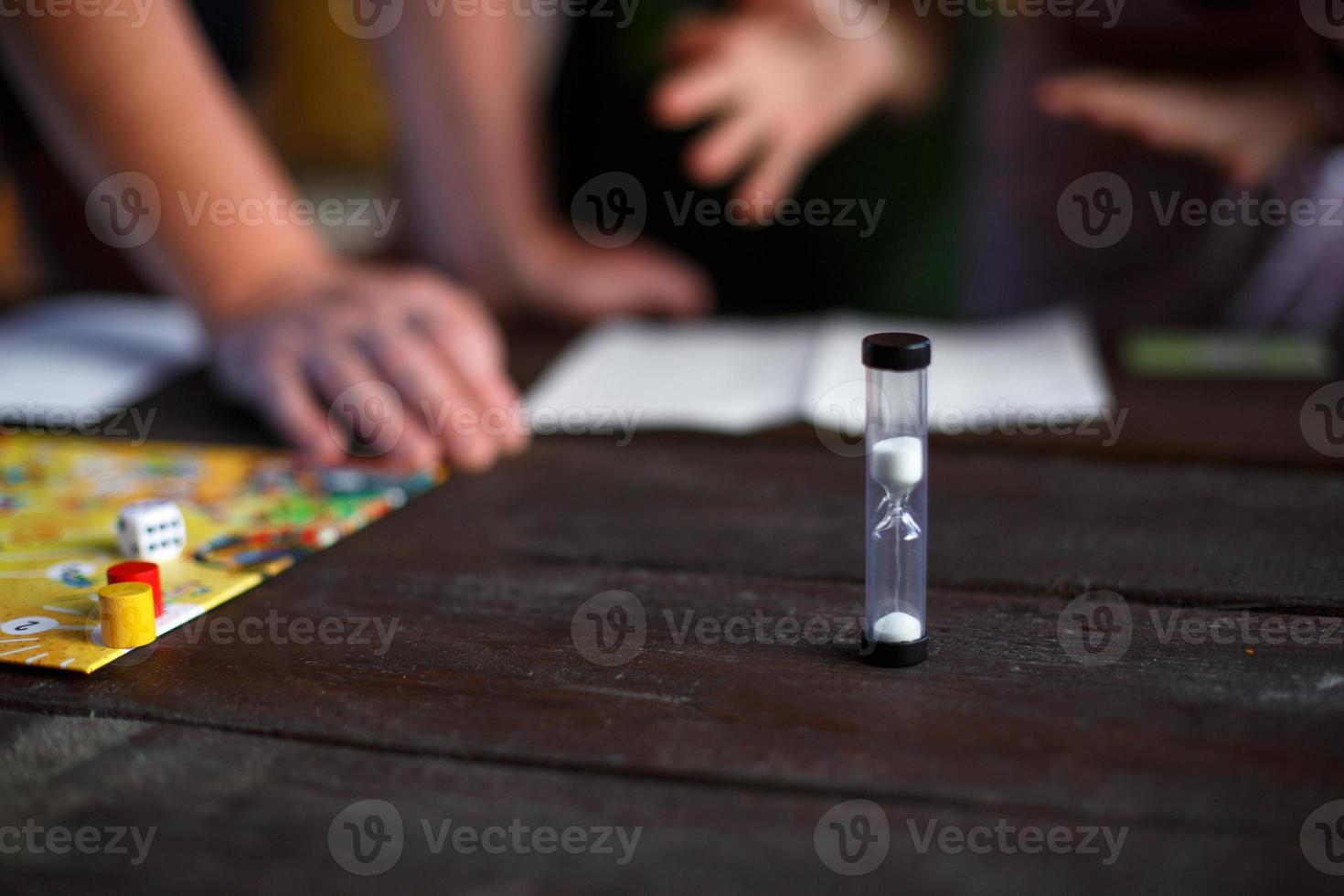 Brettspielbrett, Chips, Würfel, Timer auf einem dunklen Holztisch und Hände im Hintergrund. das konzept der teamarbeit, der intellektuellen entspannung, der firmenveranstaltung, des spielens zu hause mit kindern. Platz kopieren foto