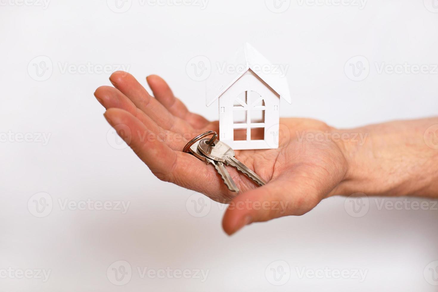 Schlüsselanhänger mit Hausschlüsseln an der Hand eines Mannes auf weißem Hintergrund. Immobilienmakler, Verkauf neuer Häuser, Hypotheken, Umzug, Bankwesen, Reparatur und Bau foto