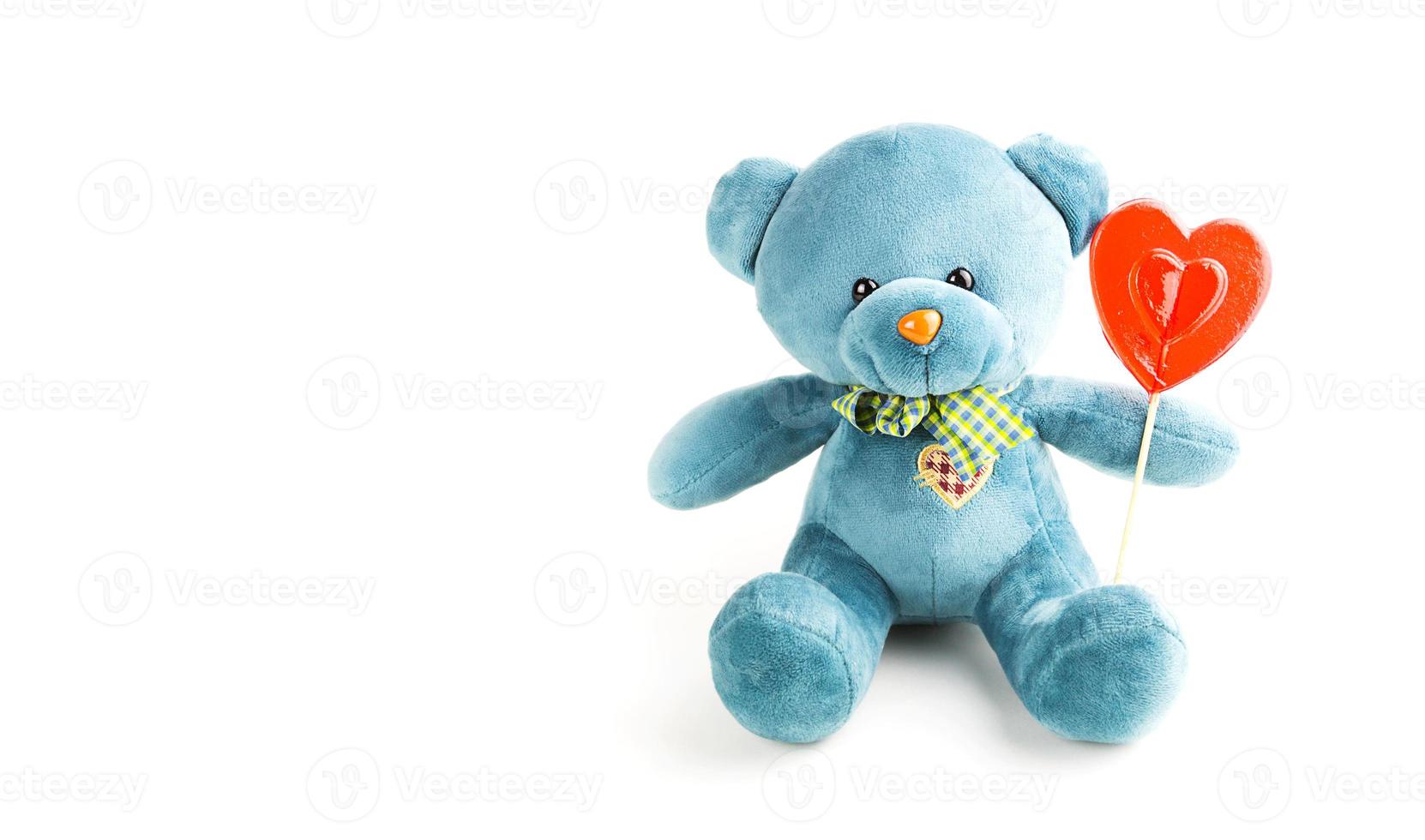 türkisfarbener weicher Teddybär mit rotem Lollipop-Herz auf einem Stock auf weißem Hintergrund. Liebe, ein Geschenk an ein Mädchen, eine Liebeserklärung, Valentinstag. Platz kopieren foto