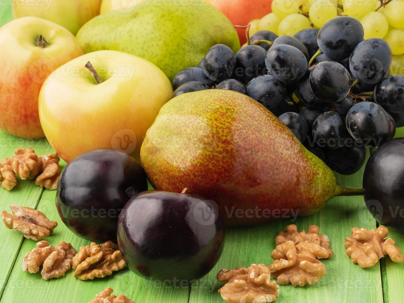 Satz Früchte auf einem grünen Holztisch - Äpfel, Birnen, Trauben, Pflaumen, Walnüsse foto