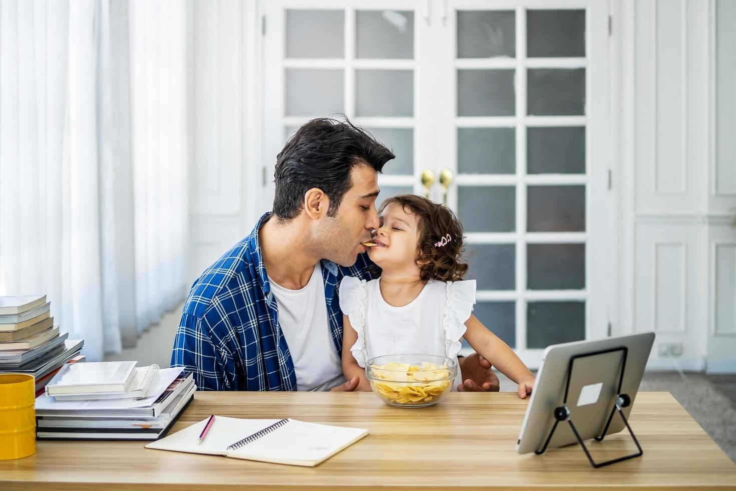 junger vater der kaukasischen familie, der zusammen mit der kleinen tochter kartoffelchips im berg isst und bildungs-online-programm der karikaturen anschaut foto