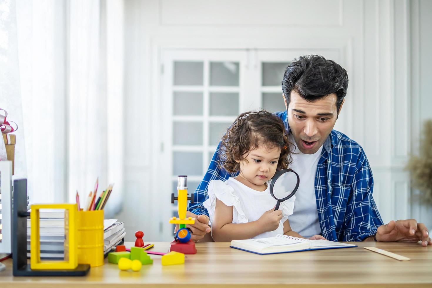 Kleines Mädchen, das wissenschaftliche Experimente im Labor mit Vater durchführt, der durch die Lupe schaut. vater und tochter studieren biologie- und chemieunterricht mit mikroskop. häuslicher Unterricht foto