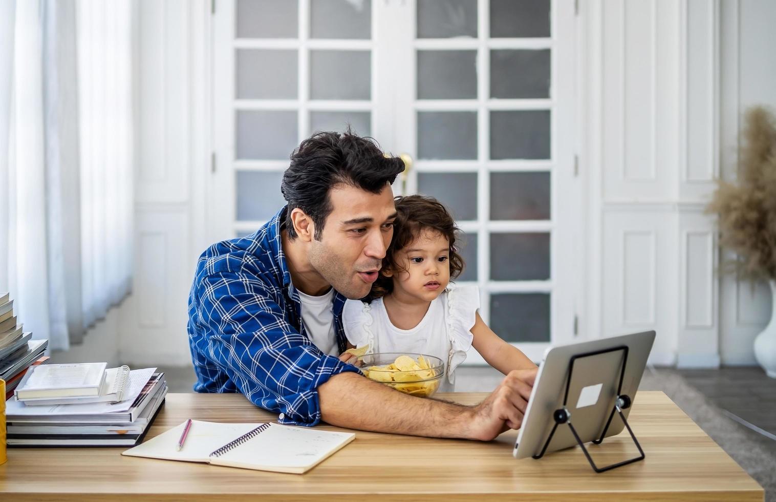 junger attraktiver vater und kleine süße tochter, die sich das filmvideo auf dem tablet ansehen und zu hause mit glück kartoffelchips essen. foto