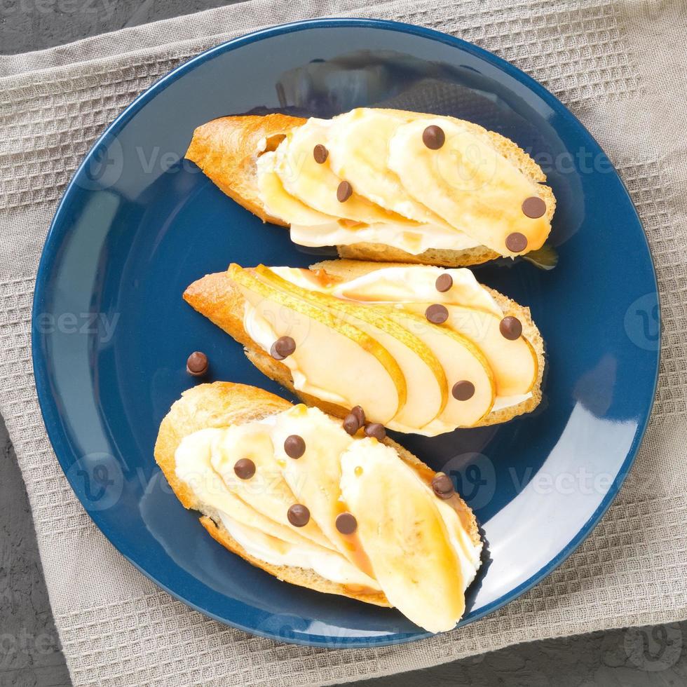 blauer teller mit drei köstlichen französischen toast mit bananen, birnen, frischkäse, schokoladendrops, karamellsirup, draufsicht foto