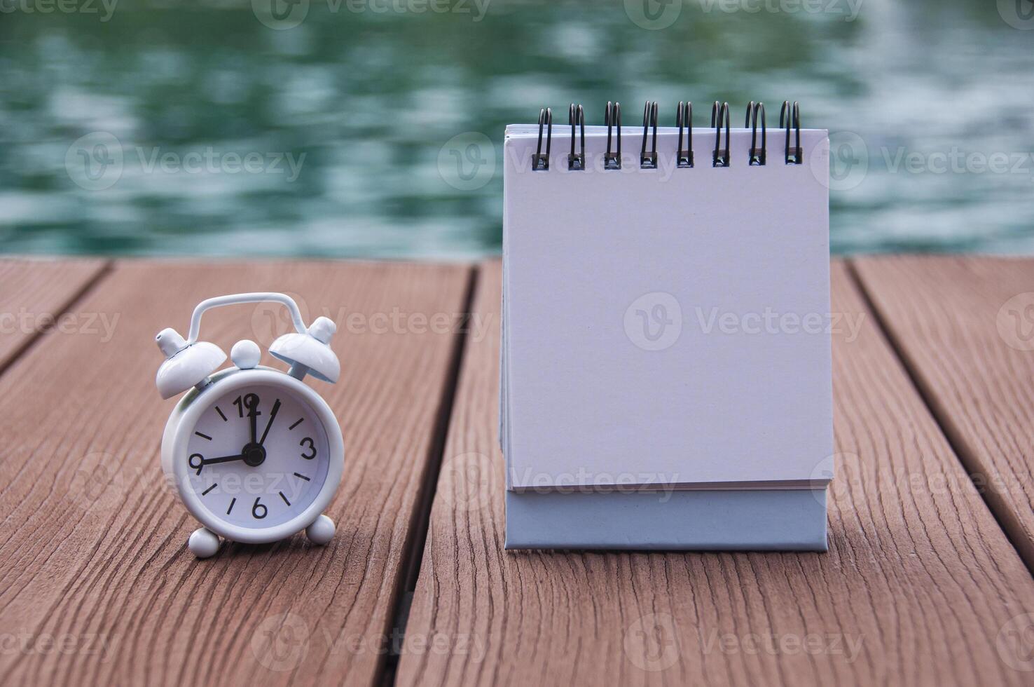 wecker auf holzboden mit leerem notizblock. mit Schwimmbadhintergrund. die Uhr auf 9 Uhr gestellt. foto