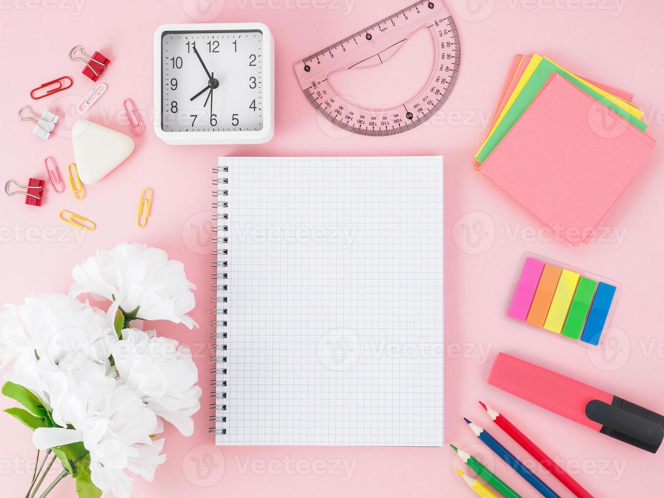 Blick von oben auf den rosafarbenen Bürodesktop mit Notizbuch im Käfig, Blumen, Schulmaterial auf dem Tisch, Platz für Text. zurück zum schulkonzept. foto