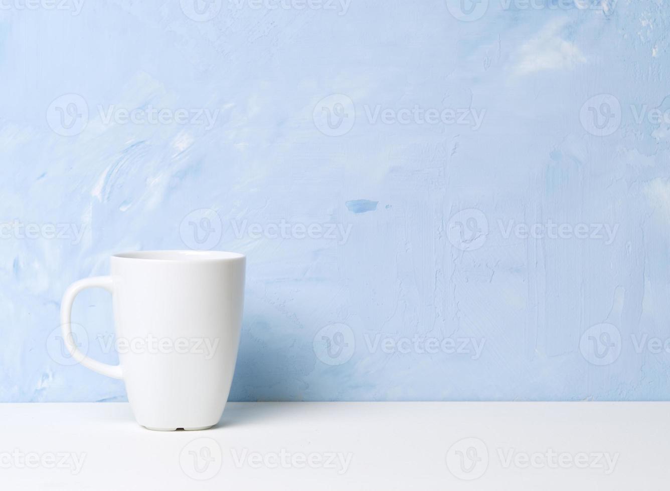 Weiße Tasse mit Tee oder Kaffee auf einem weißen Tisch gegenüber einer hellblauen Betonwand. foto