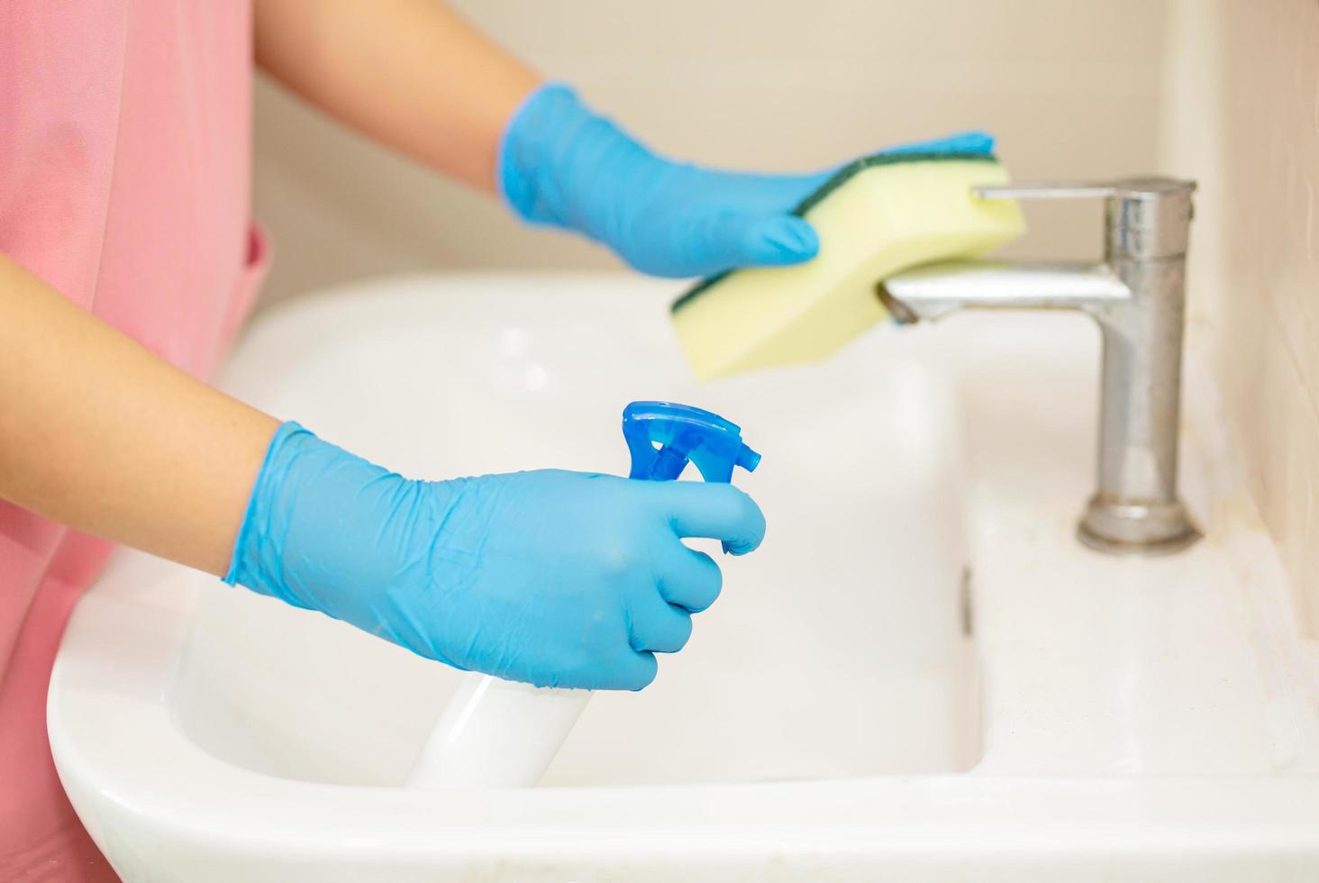 Person, eine Hand in einem blauen Gummihandschuh auf dem Bild, entfernt und wäscht das Waschbecken im Badezimmer foto