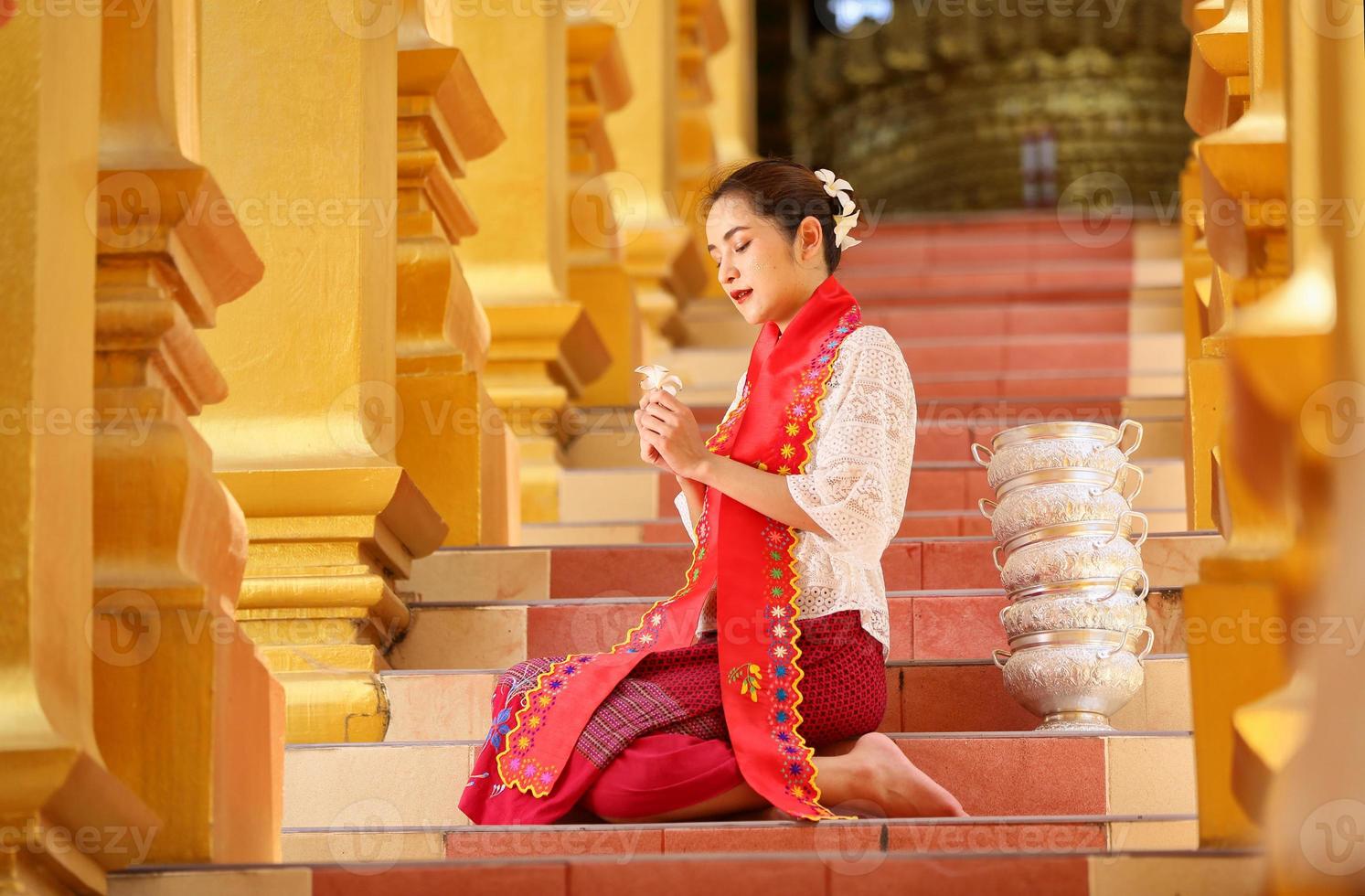 Junges asiatisches Mädchen in traditioneller burmesischer Tracht, das eine Schüssel Reis in der goldenen Pagode im Tempel von Myanmar hält. myanmarer frauen, die blumen mit birmanischer traditioneller kleidung halten, die einen buddhistischen tempel besuchen foto