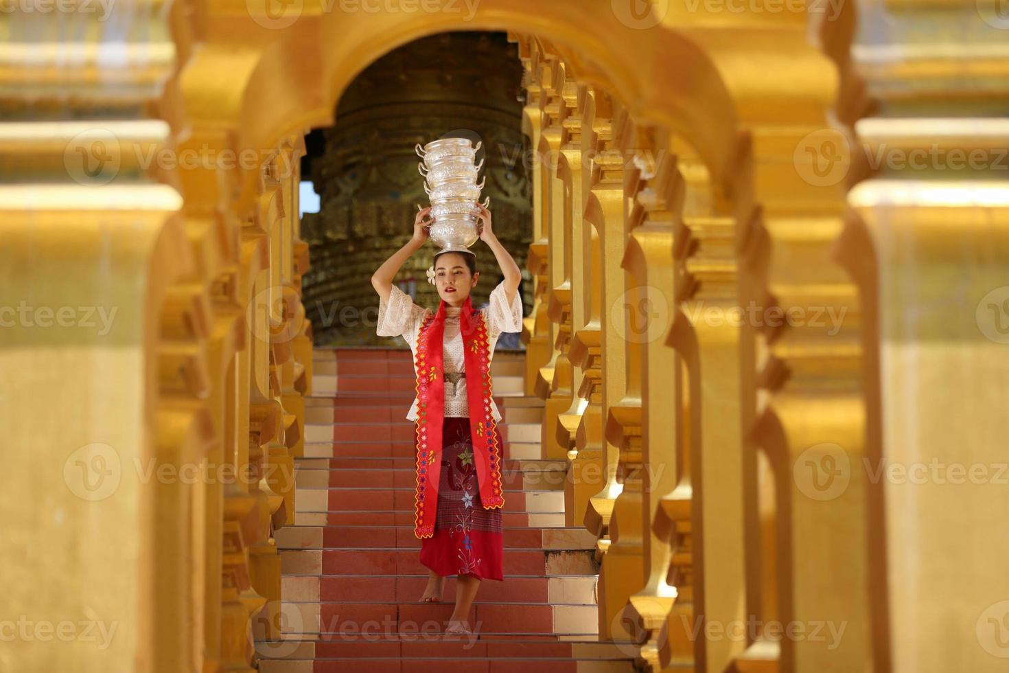 Junges asiatisches Mädchen in traditioneller burmesischer Tracht, das eine Schüssel Reis in der goldenen Pagode im Tempel von Myanmar hält. myanmarer frauen, die blumen mit birmanischer traditioneller kleidung halten, die einen buddhistischen tempel besuchen foto