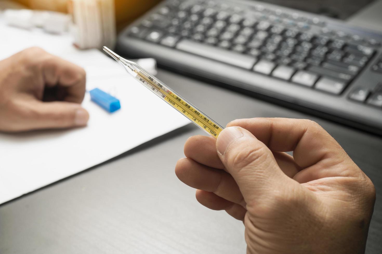 Männer halten klinisches Thermometer in der Hand auf dem Schreibtisch, nachdem sie das klinische Thermometer benutzt haben und sich Sorgen über die Ausbreitung des Coronavirus machen foto