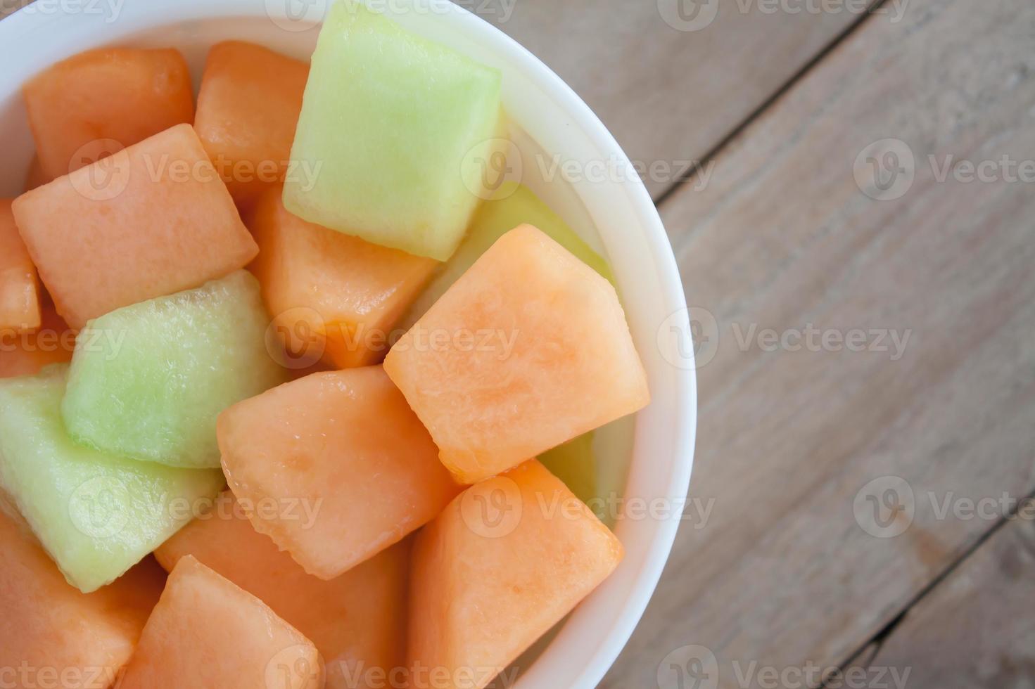 Closeup Melonenscheibe in weißer Schale mit Holztischhintergrund foto