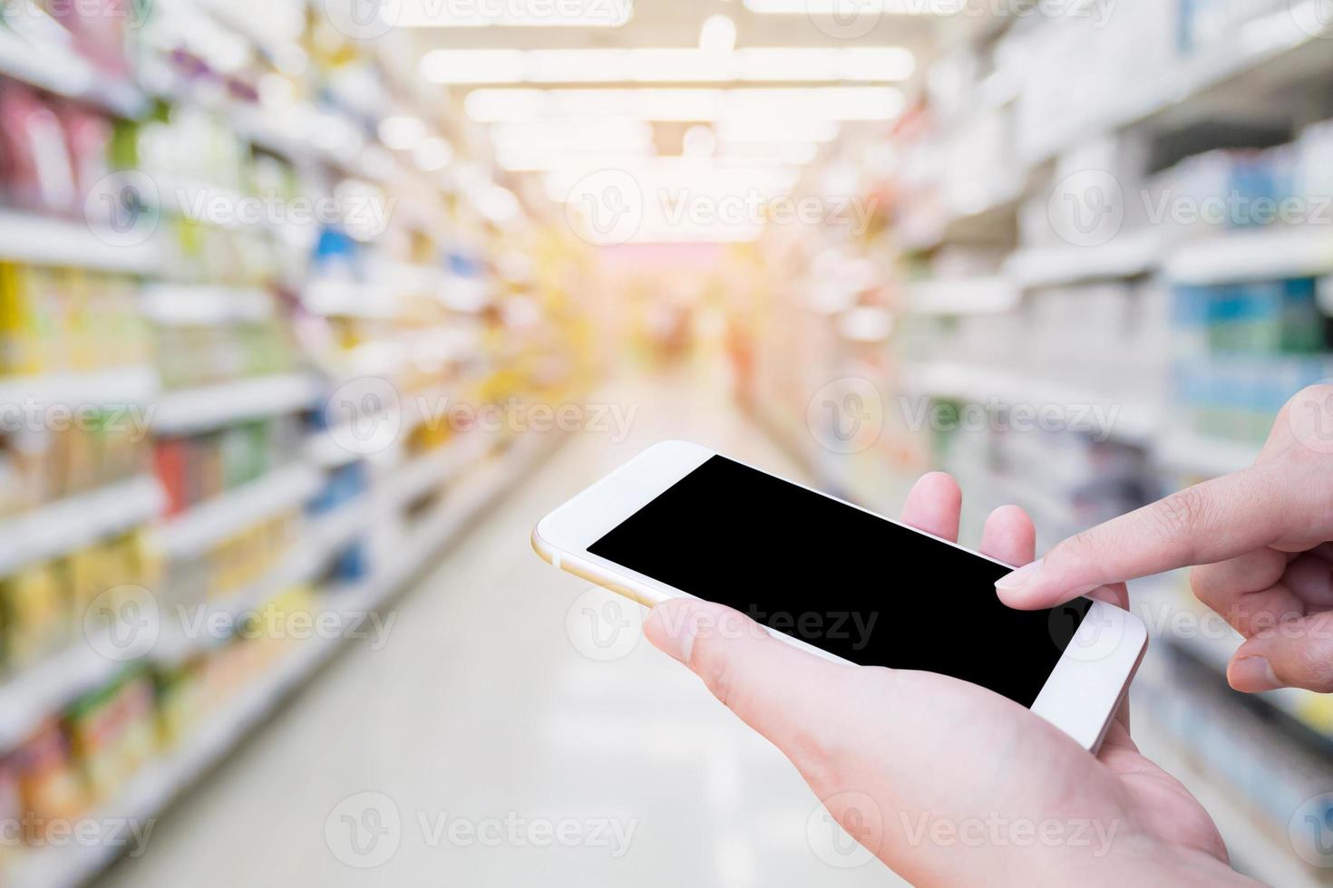 weibliche hand, die handy mit supermarkthintergrund hält foto