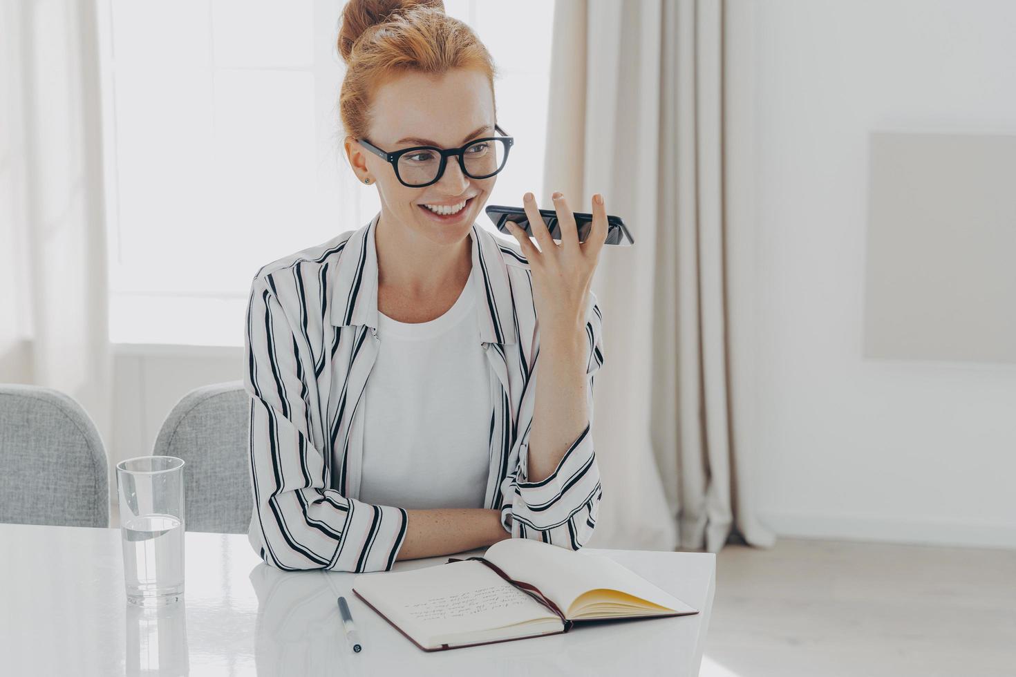 positive rothaarige frau verwendet handy-audioerkennung, um nachricht zu senden foto