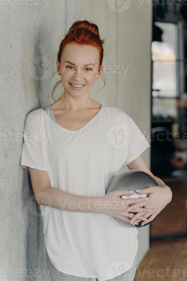 süße junge rothaarige Frau mit Pilates-Ball, die sich nach dem Training im Fitnessstudio entspannt foto