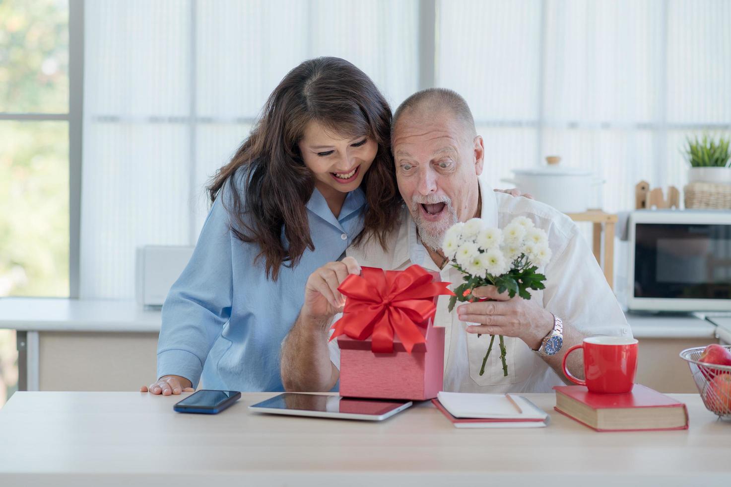 ein älteres europäisches paar und eine asiatische frau schenken sich anlässlich des valentinstages fröhlich geschenkboxen und blumen foto